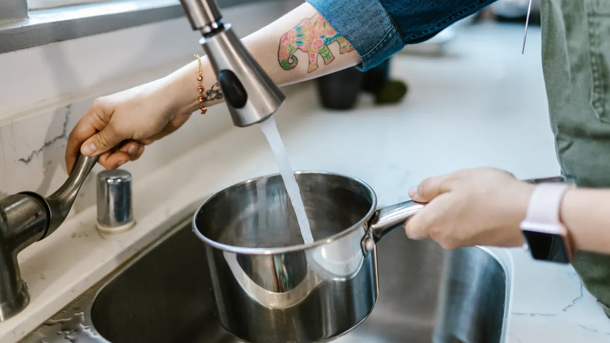Person filling a pot at a kitchen sink